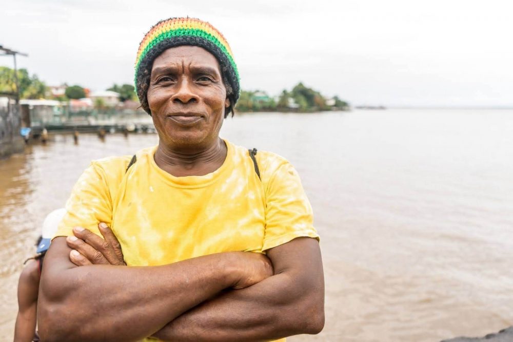 A Caribbean man in a yellow T-shirt in front of water