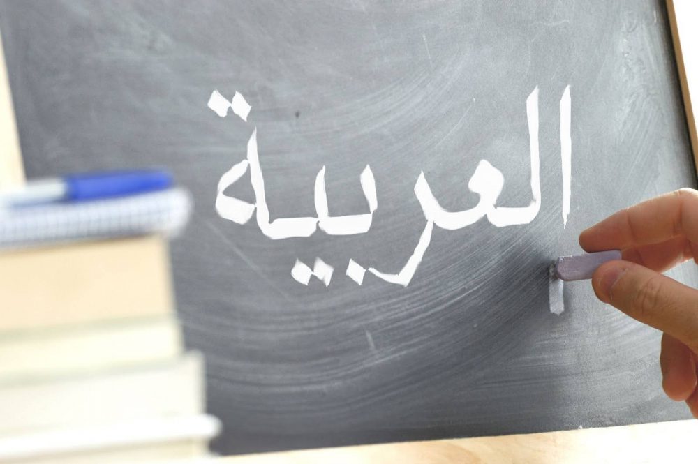 A person writing on a blackboard in Arabic