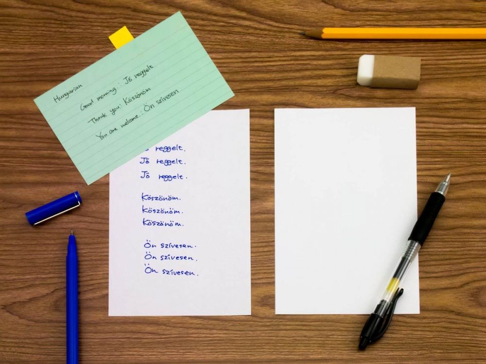 Notes for learning Hungarian, two pens, a pencil, and a rubber on a wooden surface