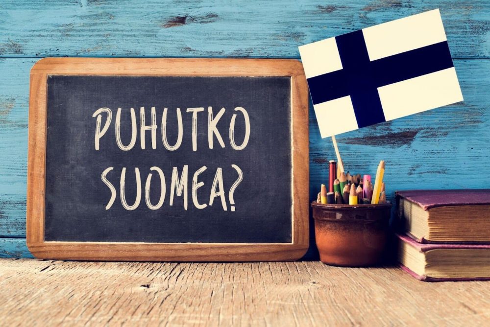 A writing in Finnish on a small blackboard next to a cup with pencils and a Finnish flag