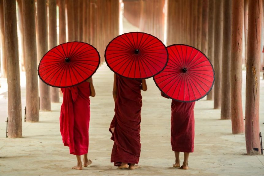 Three Buddhist monks carrying umbrellas seen from the back